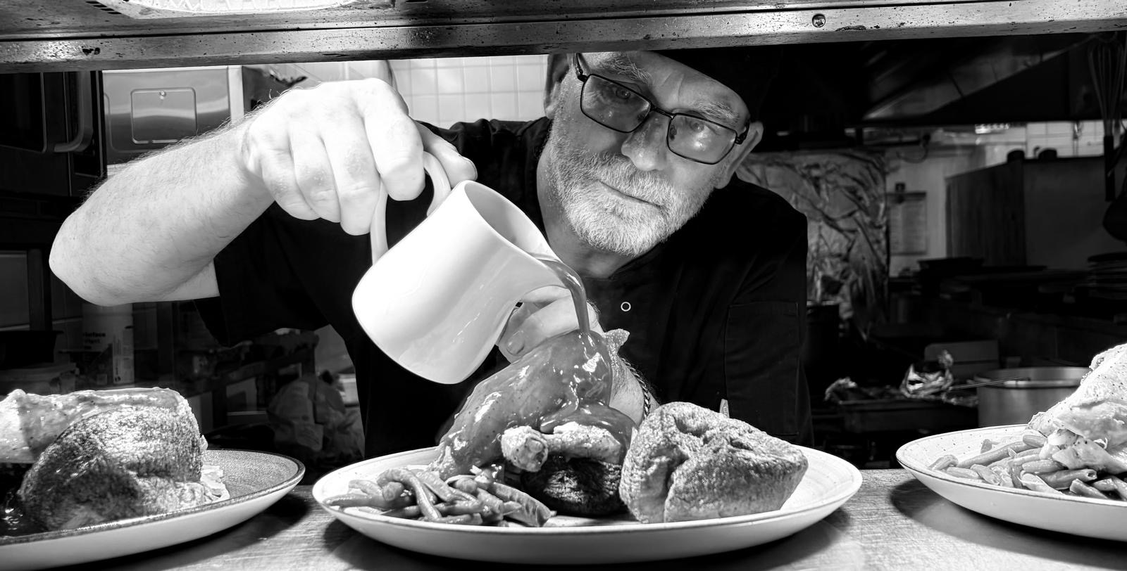Chef John Brett pouring gravy over a plated roast dinner